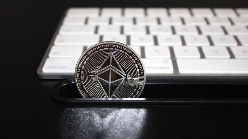 Una moneda de ethereum al lado de un teclado de ordenador.